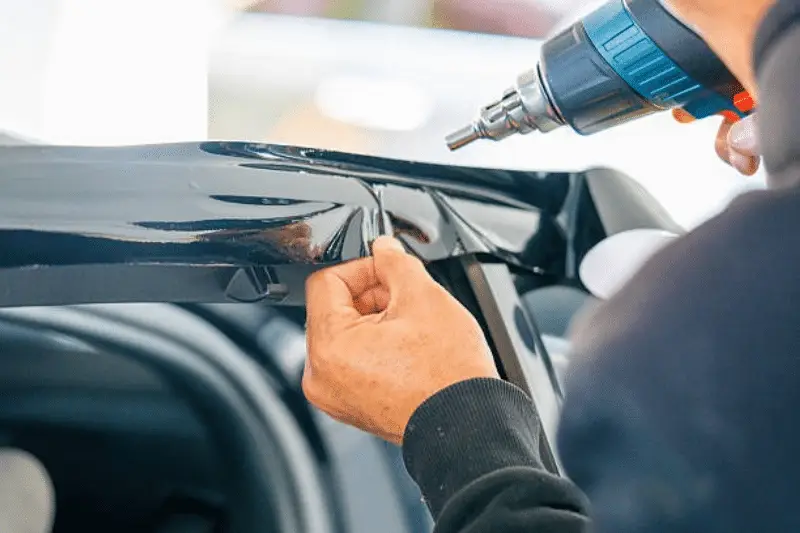 Installing black paint protection film PPF on car trim using a heat gun;  